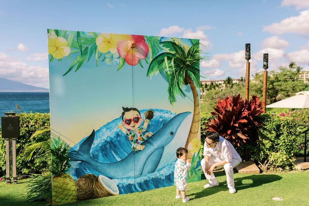 Illustrated whale backdrop with guest and toddler on the Maui lawn