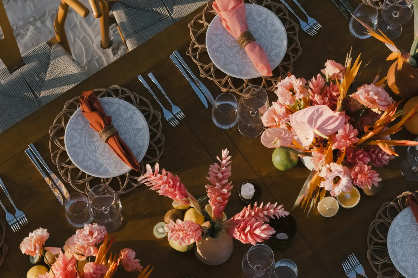 Overhead view of a beachside tablescape with coral ginger blooms, woven chargers, and citrus