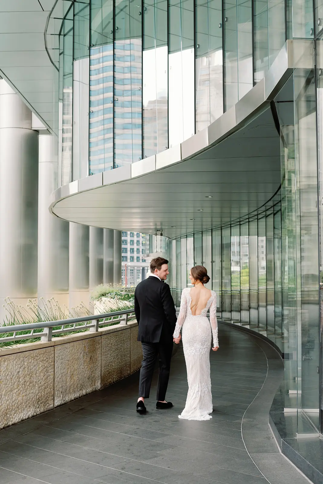 Newlyweds walking hand in hand through a glass atrium at a wedding planned by Michigan Avenue Events