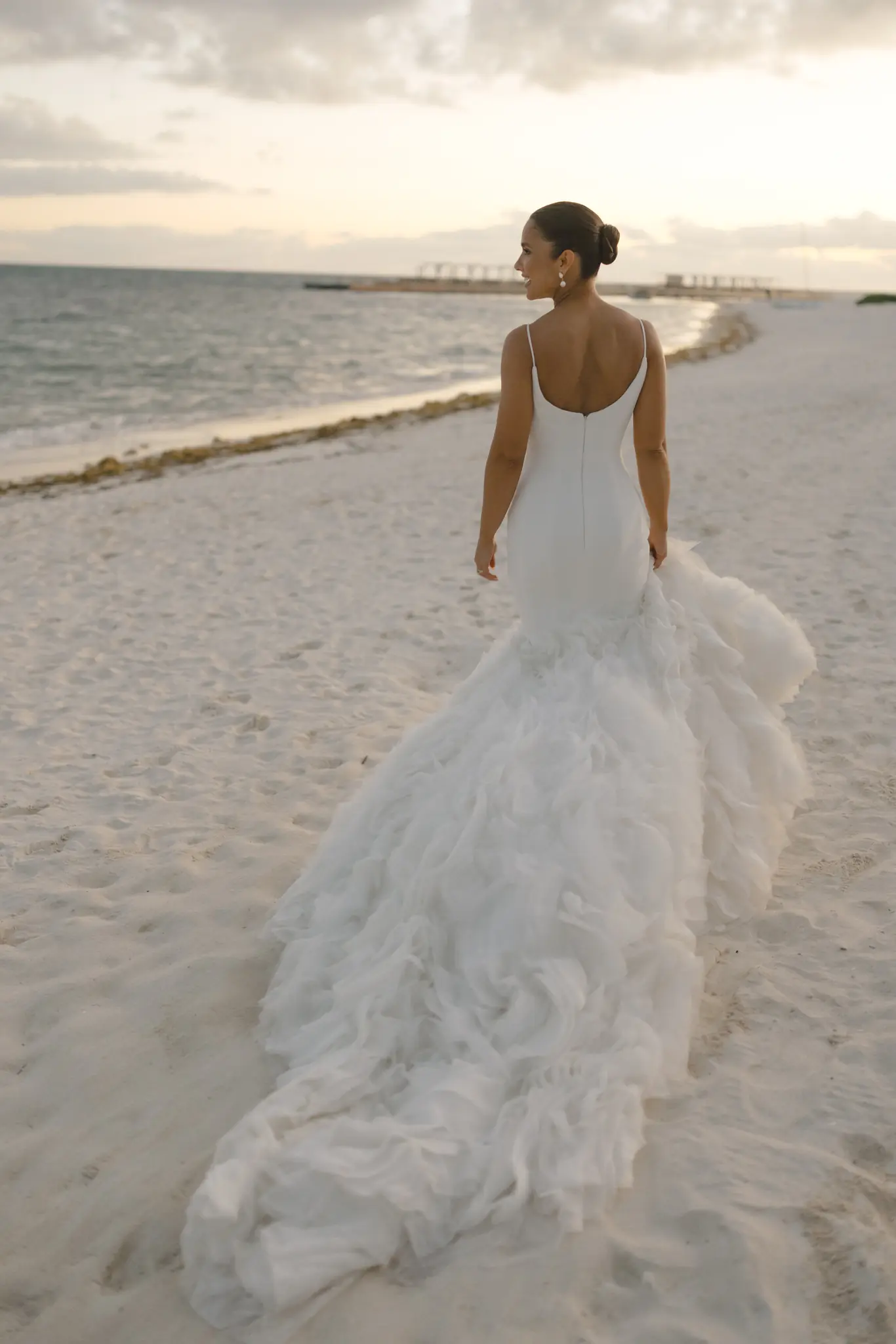 Bride in a feathered gown standing at the shoreline at a destination wedding planned by Michigan Avenue Events
