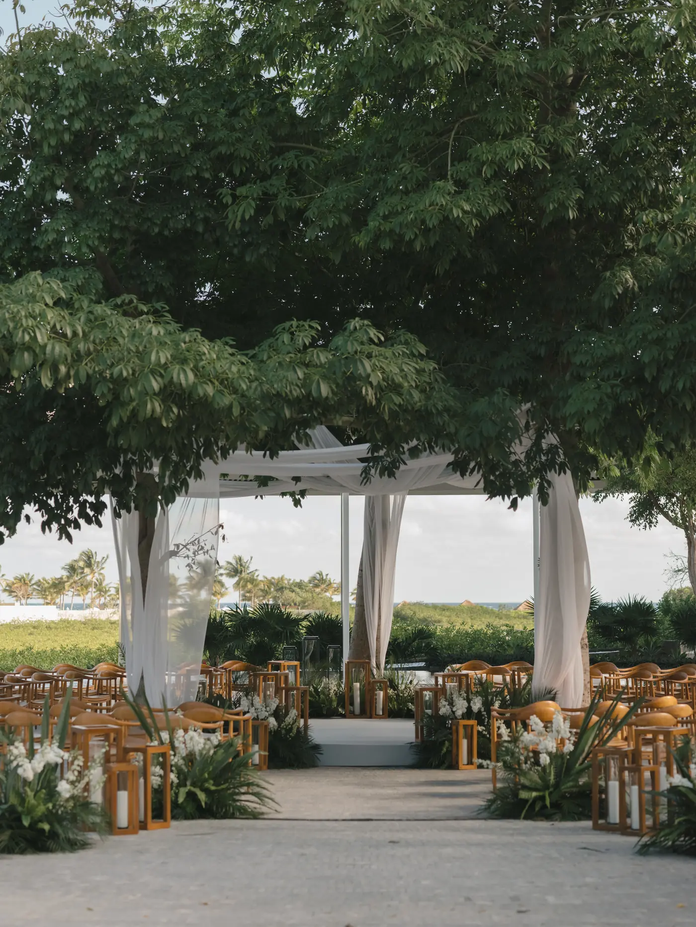 Garden ceremony aisle of white chairs and coral florals framed by trees at a destination wedding planned by Michigan Avenue Events