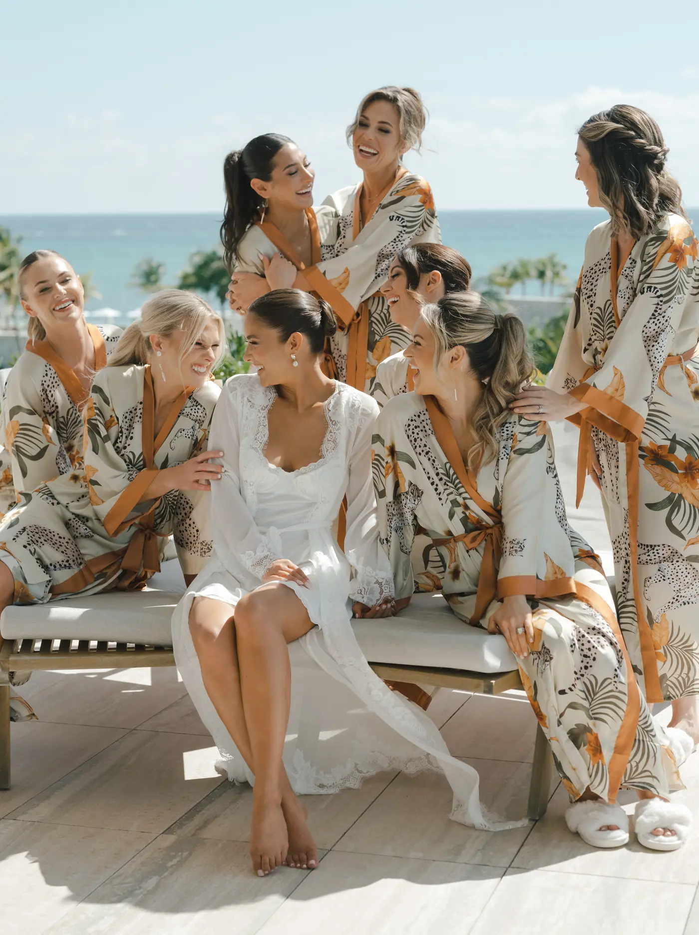 Bridesmaids in floral robes laughing on a beachside daybed before a destination wedding planned by Michigan Avenue Events