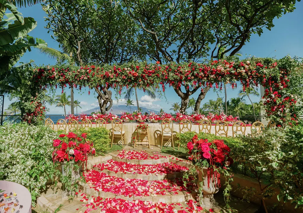 Outdoor ceremony aisle scattered with red petals beneath a floral canopy at a wedding planned by Michigan Avenue Events