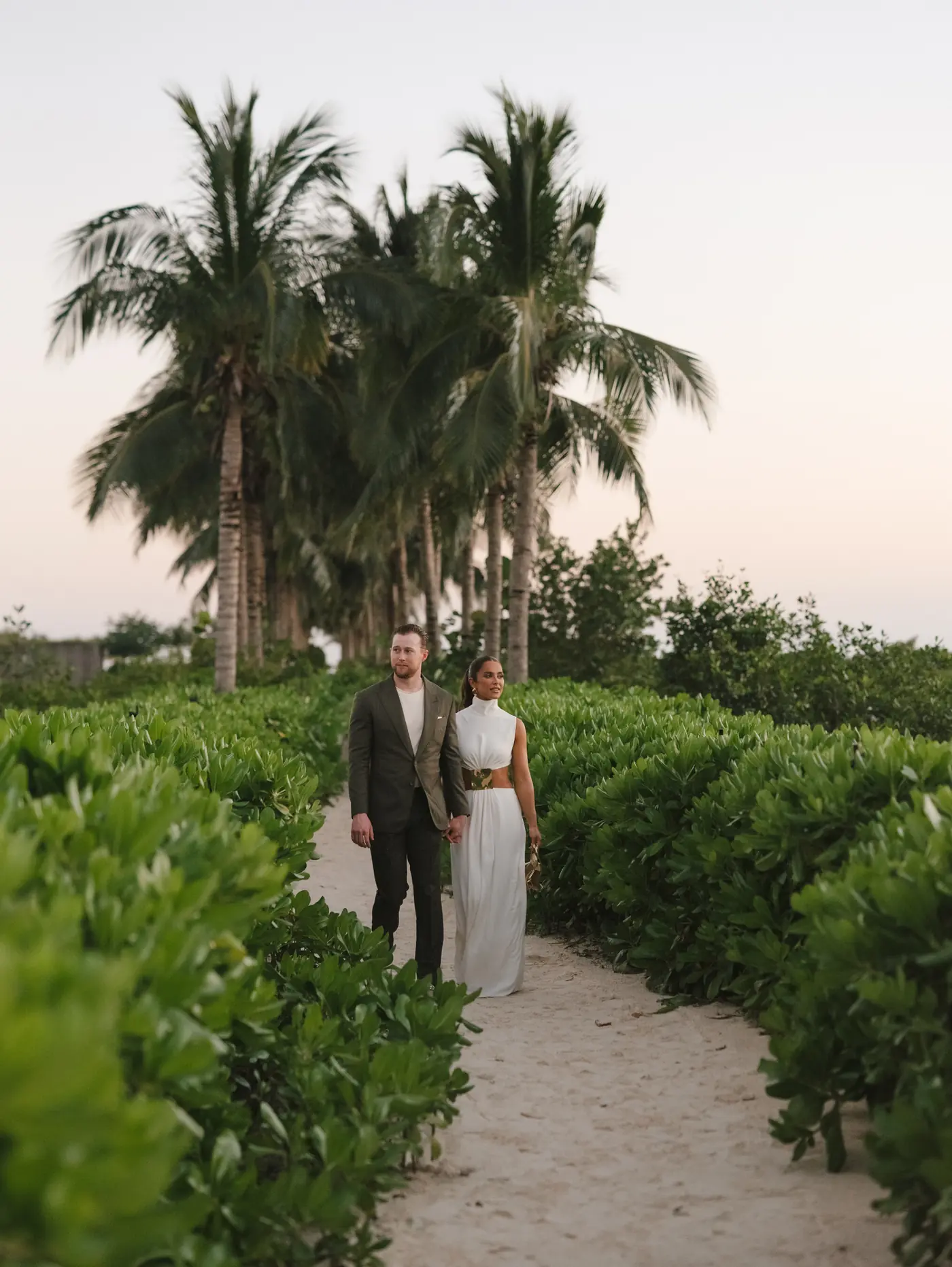 Couple strolling a palm-lined path toward the ocean at a destination wedding planned by Michigan Avenue Events