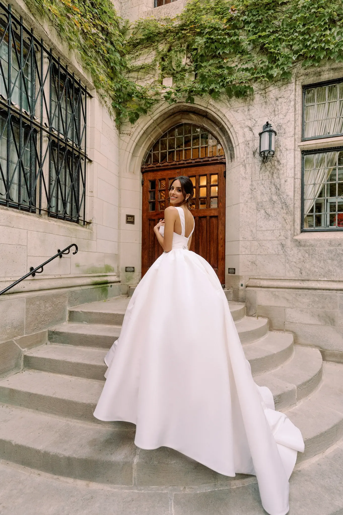 Bride in a ballgown on the ivy-framed steps of a collegiate Gothic building at a Chicago wedding planned by Michigan Avenue Events