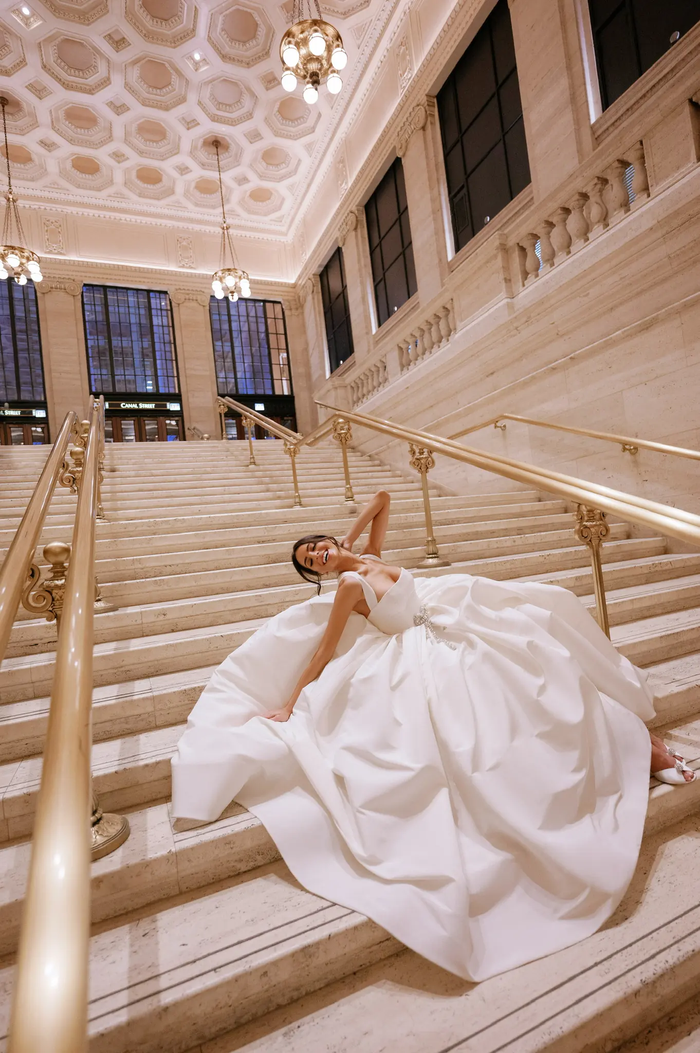 Bride posed on a sweeping marble staircase beneath a bronze balustrade at a Chicago wedding planned by Michigan Avenue Events