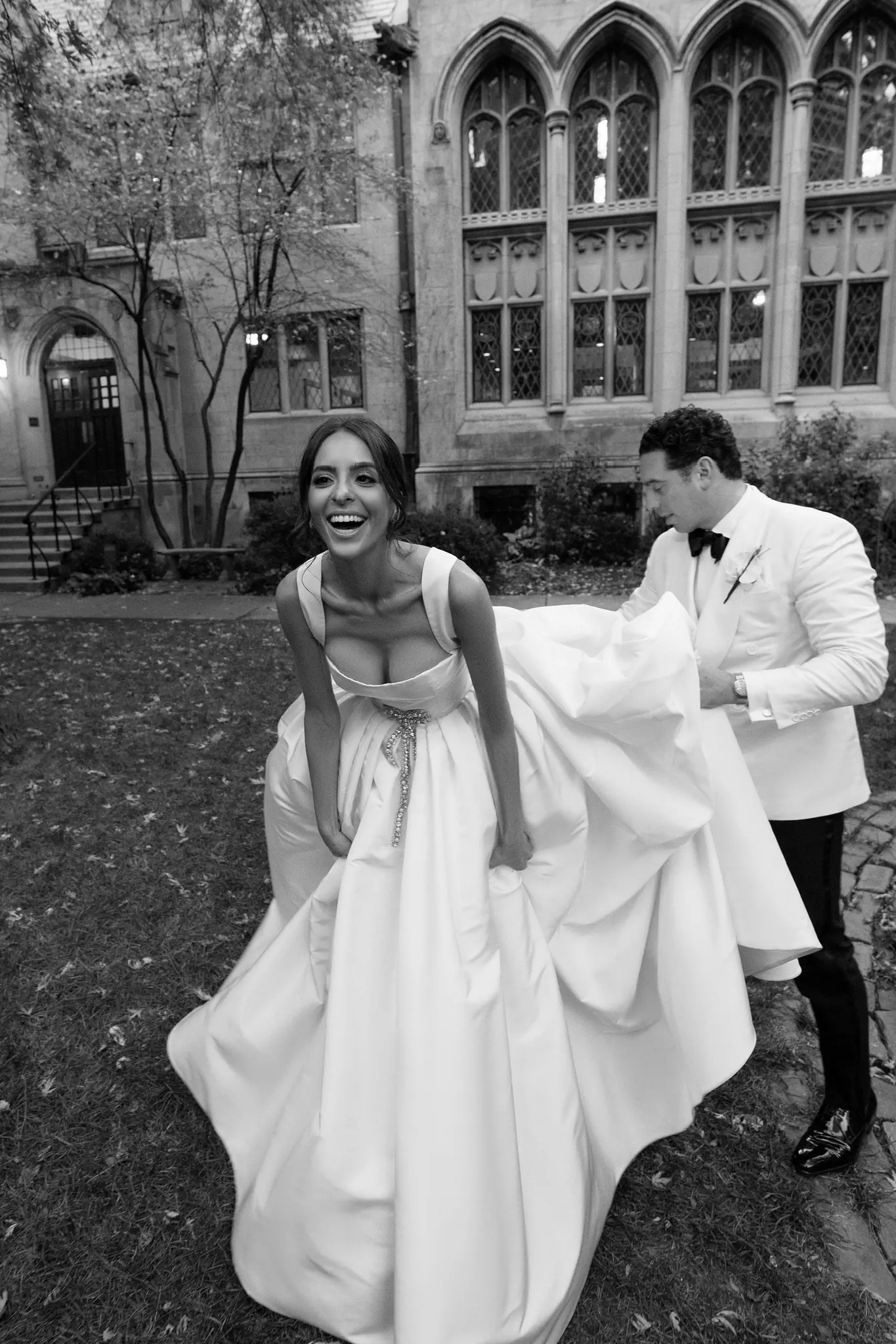 Black-and-white portrait of a couple laughing on a Gothic campus lawn at a Chicago wedding planned by Michigan Avenue Events