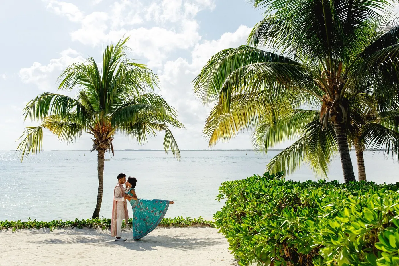Lara Sofia and Atul in traditional attire posing on the beach with palm trees
