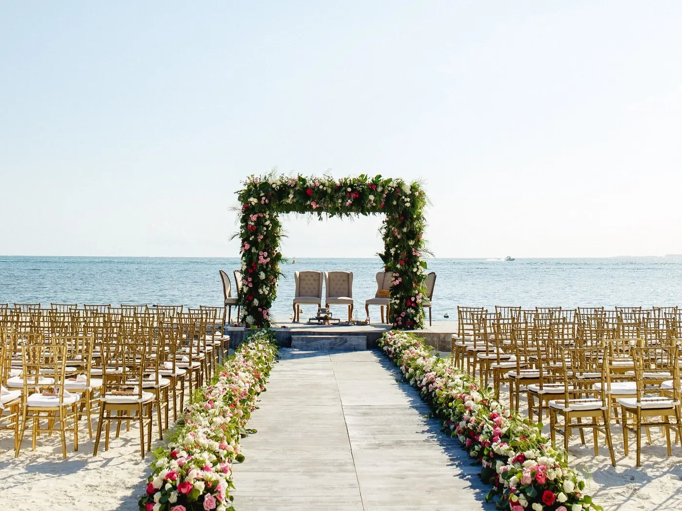 Beach mandap aisle with floral borders and gold chairs overlooking the ocean at NIZUC