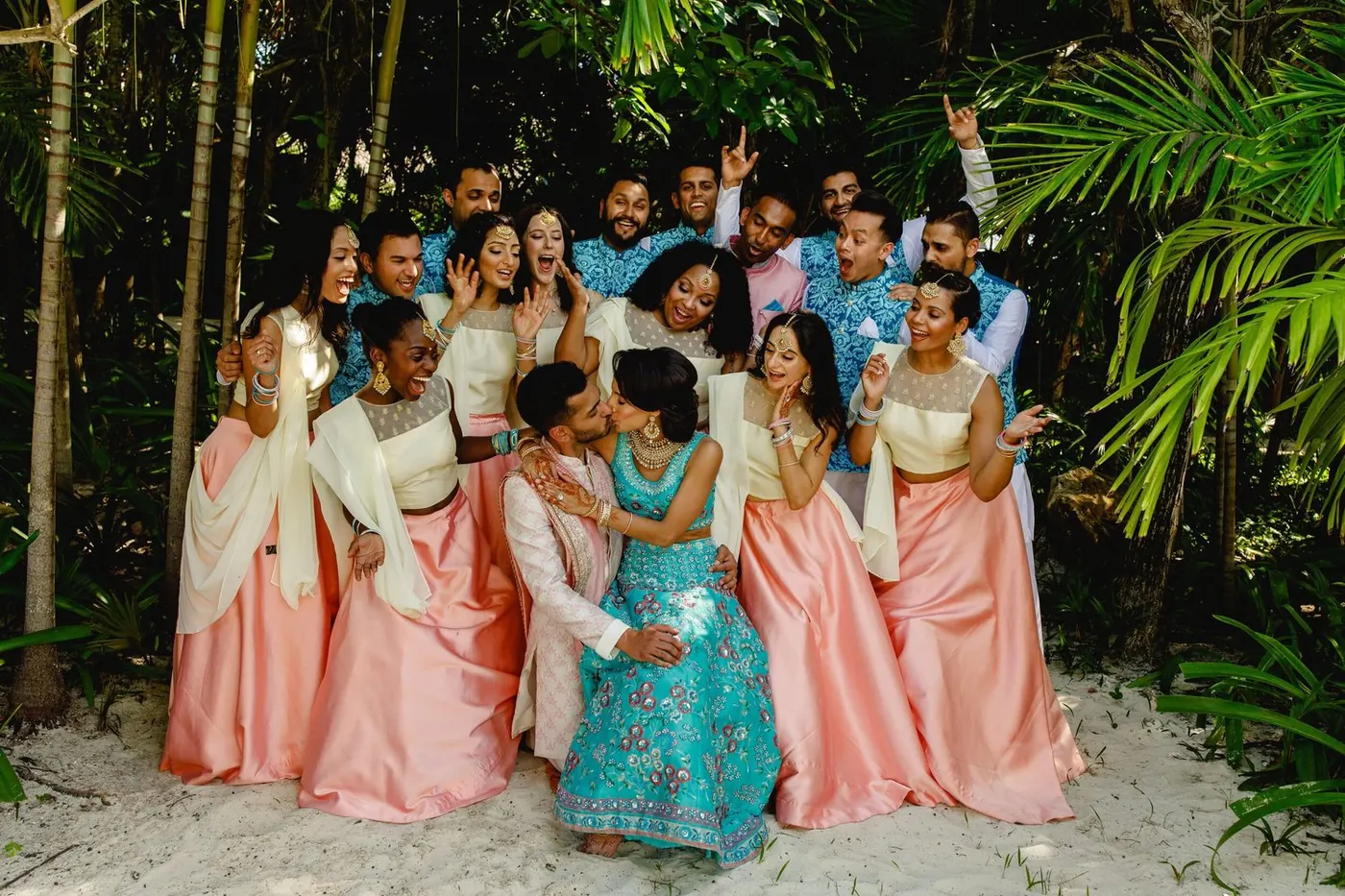 Wedding party celebrating as Lara Sofia and Atul kiss on the sand